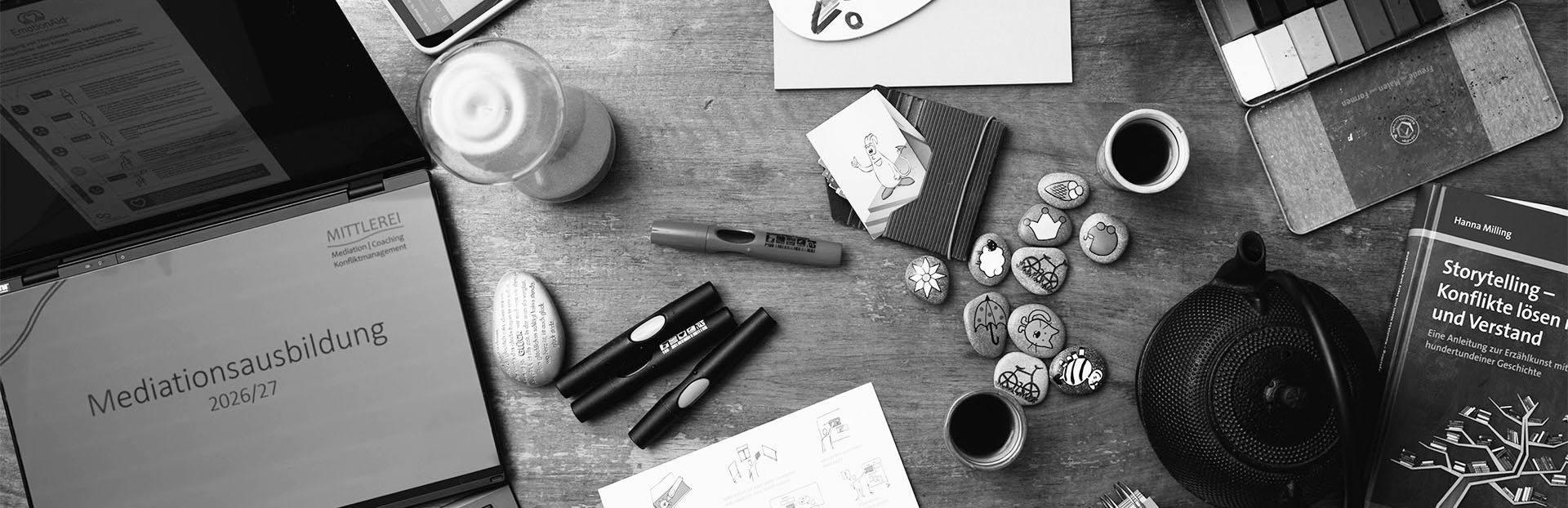 Mediationsausbildung & Workshops: Tisch mit vielen Arbeitsmaterialien zum Thema Mediation von oben gesehen: Stifte, Papier, Karten, Wachsmalblöcke, Bücher, Laptop